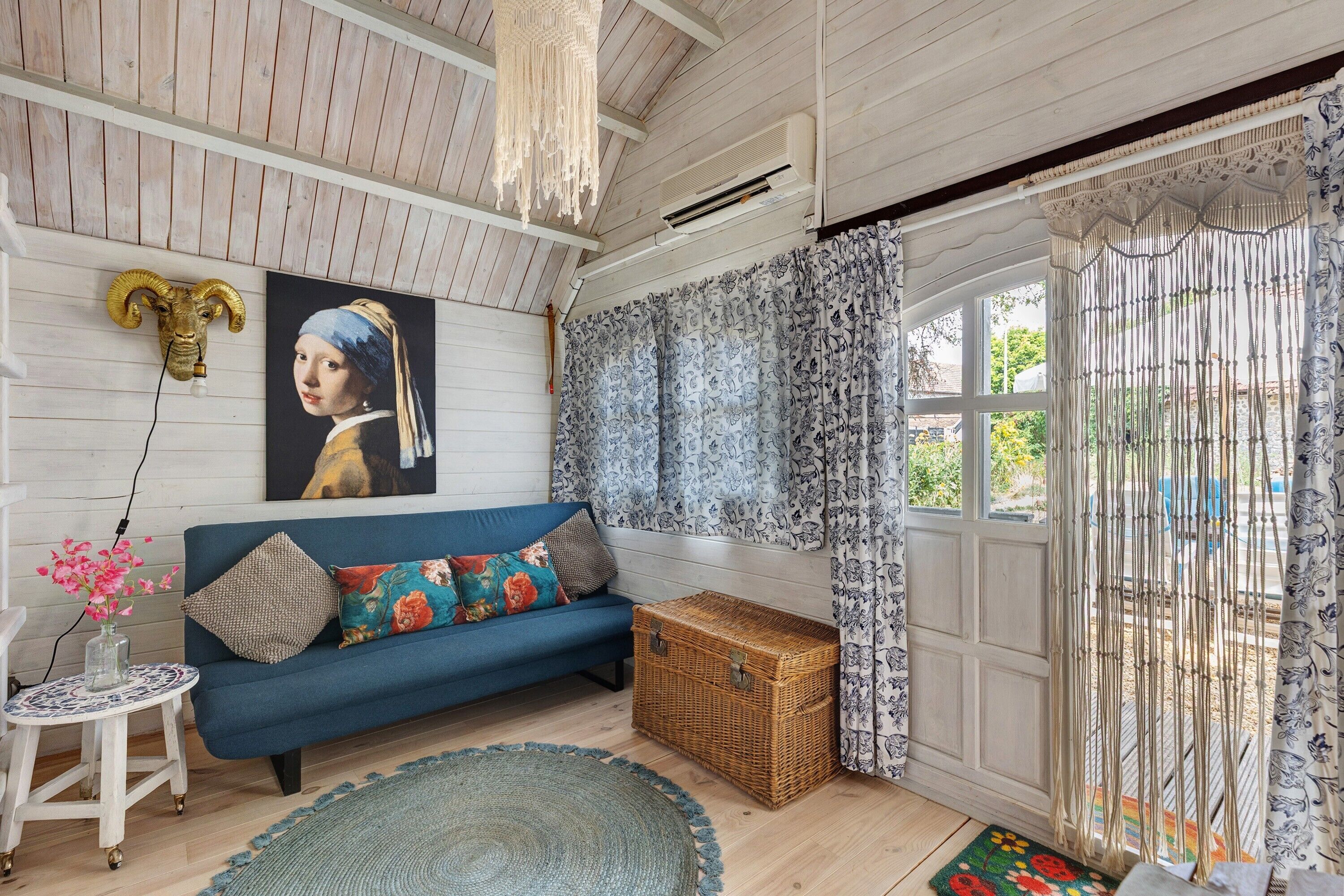 A room with a blue sofa, a decorative ram's head, a framed artwork, a wicker chest, and a patterned curtain.