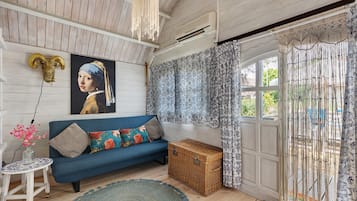A room with a blue sofa, a decorative ram's head, a framed artwork, a wicker chest, and a patterned curtain.