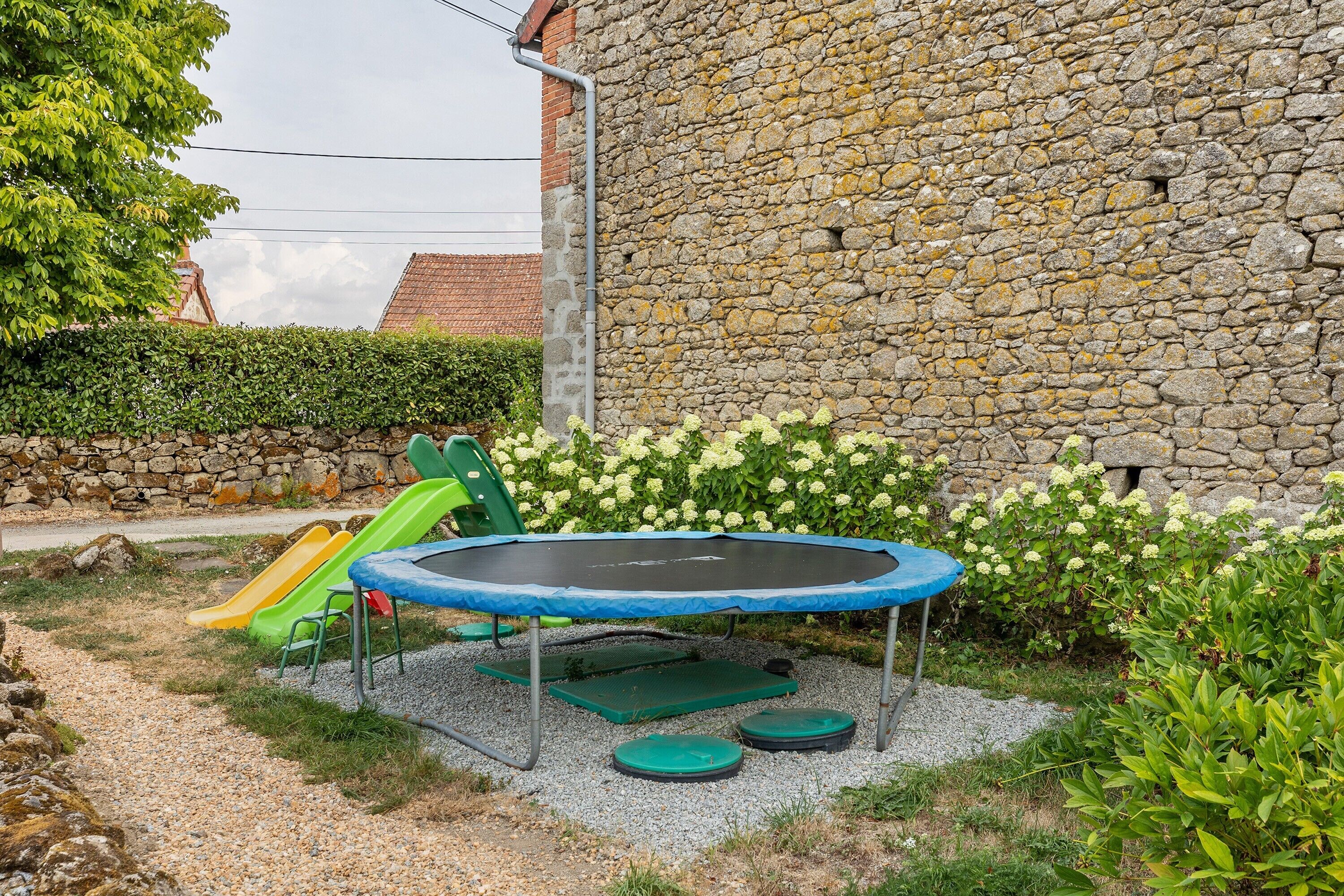 A backyard with a trampoline, a slide, and a stone wall.