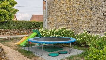 A backyard with a trampoline, a slide, and a stone wall.