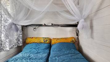 A small, single-bed room with a canopy bedspread, a power outlet, and a wall-mounted lamp.