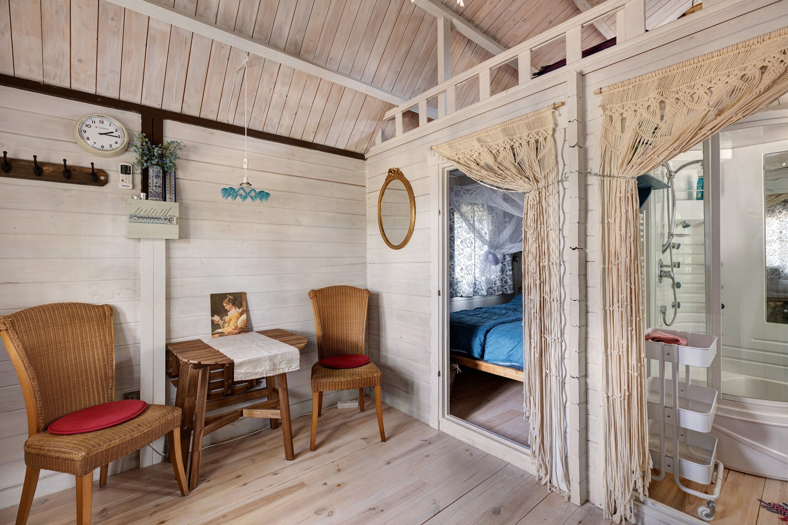 Een kamer met een bed, een tafel, twee stoelen, een klok, een spiegel en een raam met gordijnen.