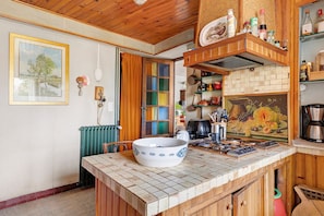 A kitchen with a tiled backsplash, wooden cabinets, a large white bowl on the counter, and various kitchen utensils and appliances.