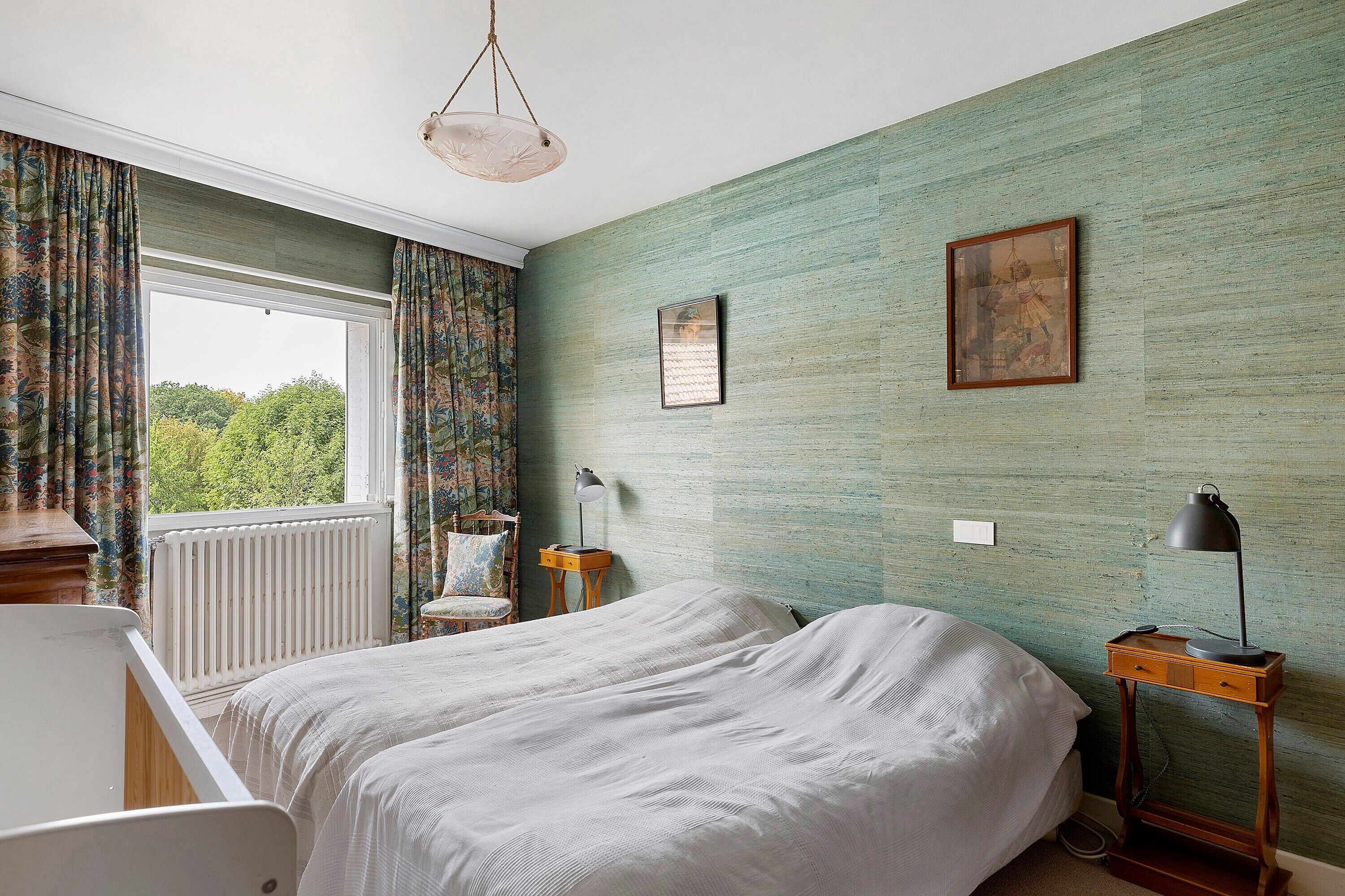 A bedroom with a bed, a chair, a nightstand, a lamp, and a window with curtains.