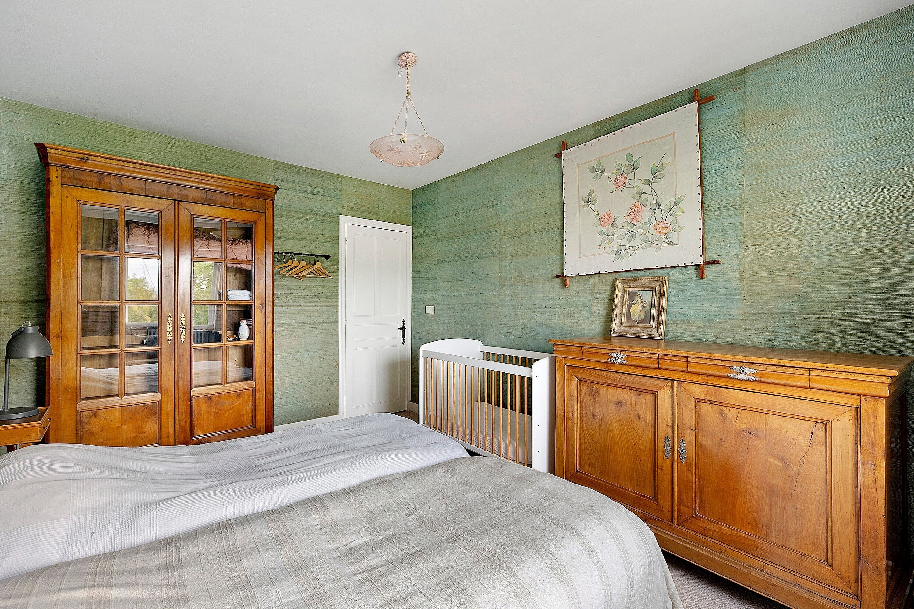 Une pièce comprenant un lit, une armoire en bois, un berceau et un luminaire suspendu.