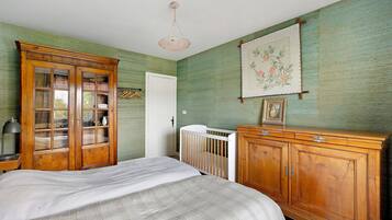 Een kamer met een bed, een houten kledingkast, een ledikant en een hanglamp.