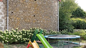 Eine Steinsäule, ein Trampolin und eine Rutsche in einem Garten.