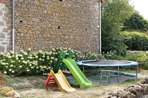 A stone wall, a trampoline, and a slide in a garden.