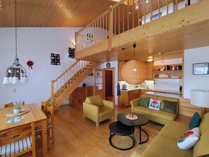 A spacious living area with a wooden staircase, a dining table, and a kitchen area. - Black Forest Happiness - My SWH Schönwald (Schönwald im Schwarzwald)