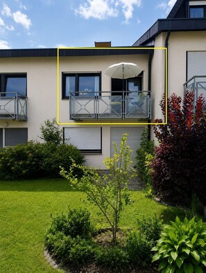 Een modern, tweelaags gebouw met een balkon, een kleine tuin en een heldere lucht.