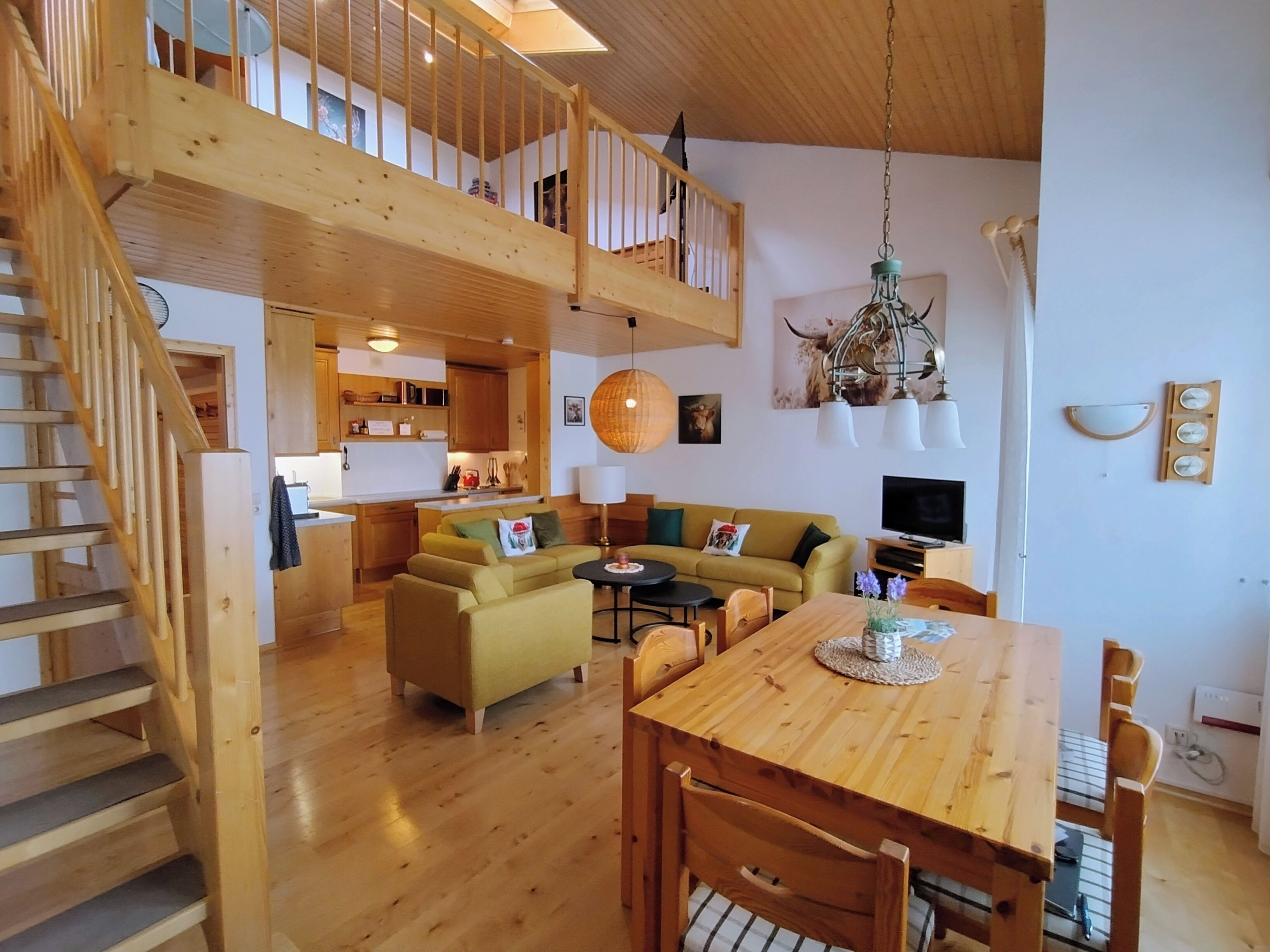 Een ruime woonkamer met een houten trap, een eettafel en een bank.
