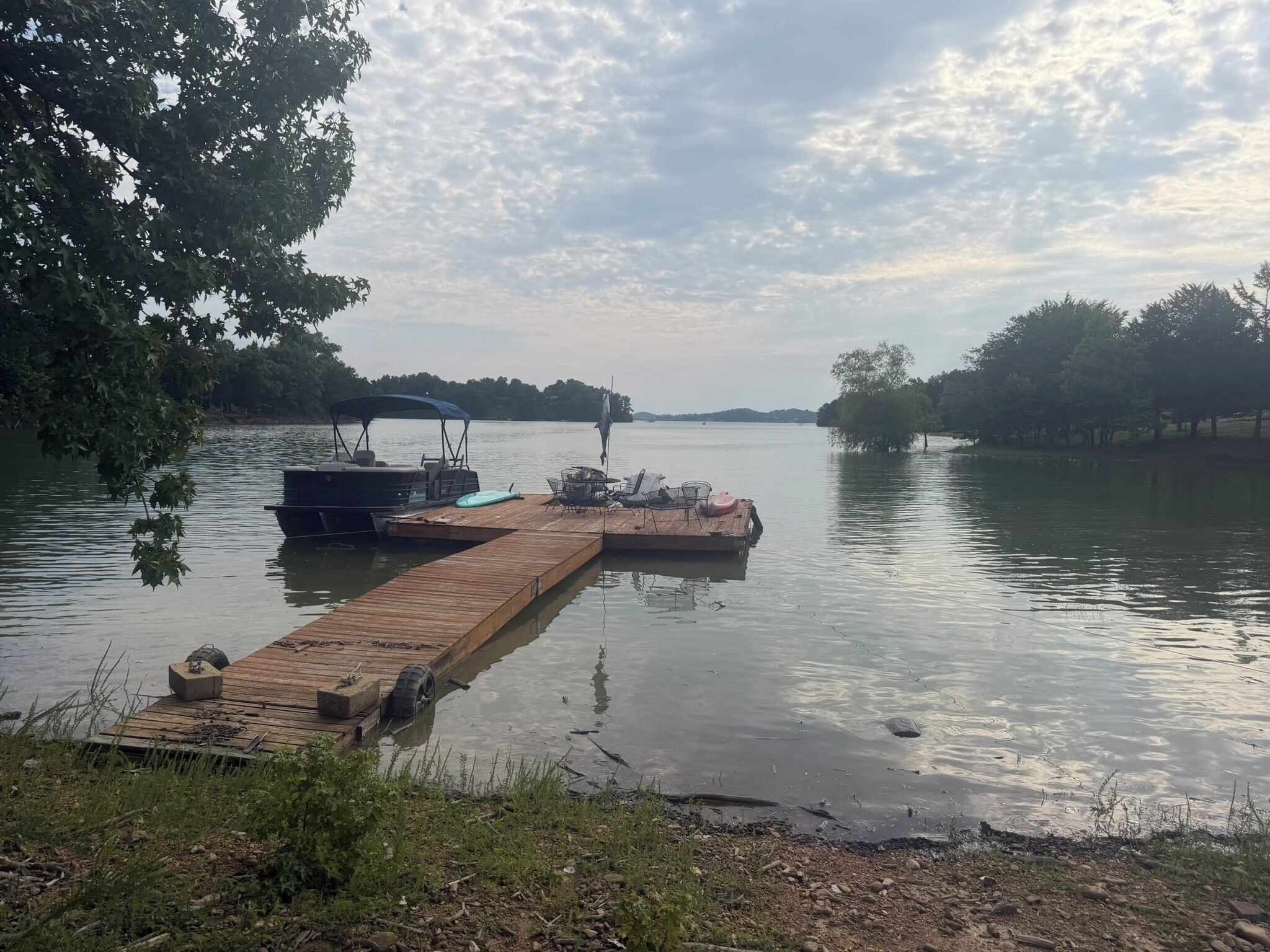 A wooden dock extending into calm water with a boat docked on the left and a small pier on the right.