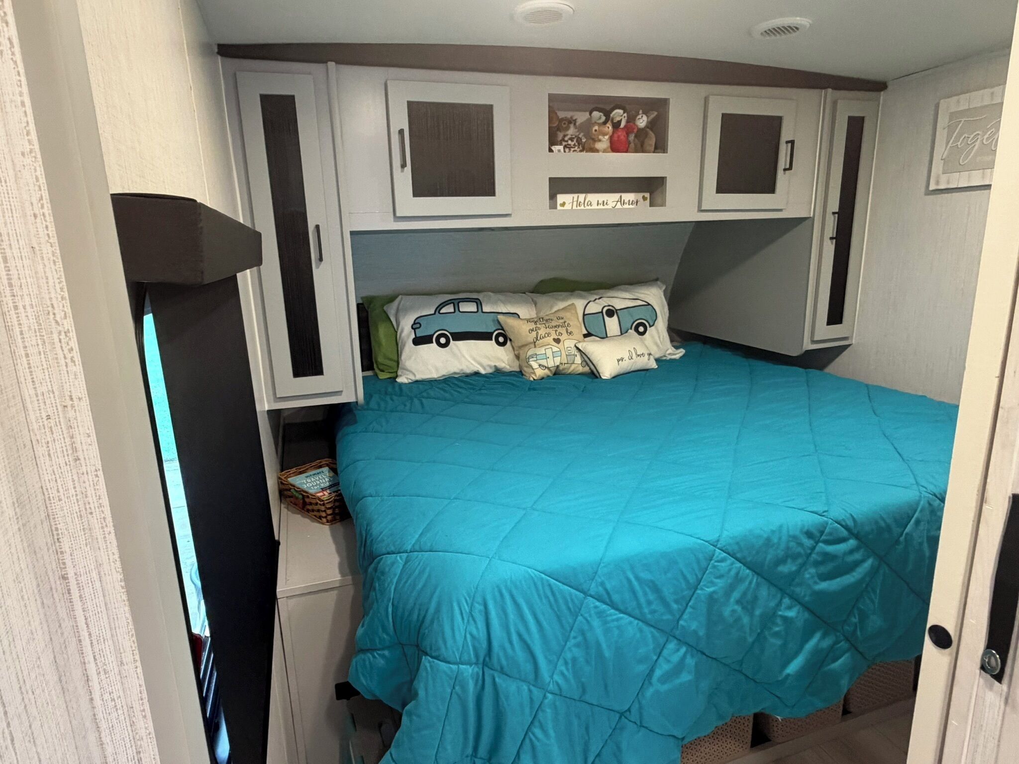 A bedroom with a teal bedspread, a small shelf with decorative items, and a door with a handle.