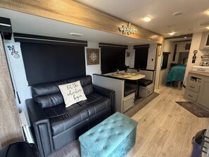 Ein kompaktes Wohnmobil-Interieur mit einer schwarzen Ledersofa, einem kleinen Tisch mit zwei Weingläsern und einer Küchenzeile.