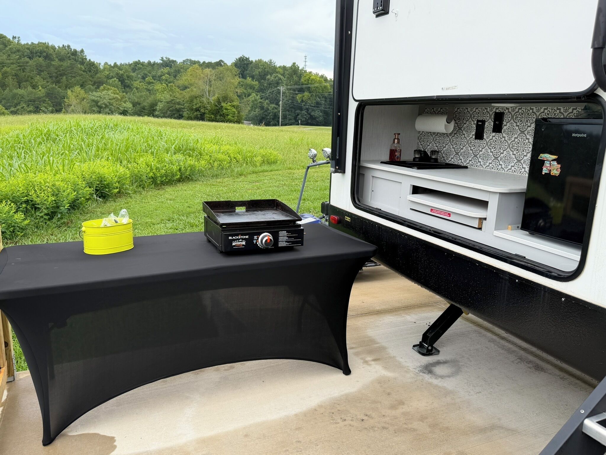 A kitchen area in a camper with a black table, a yellow bucket, and a Blackstone appliance.