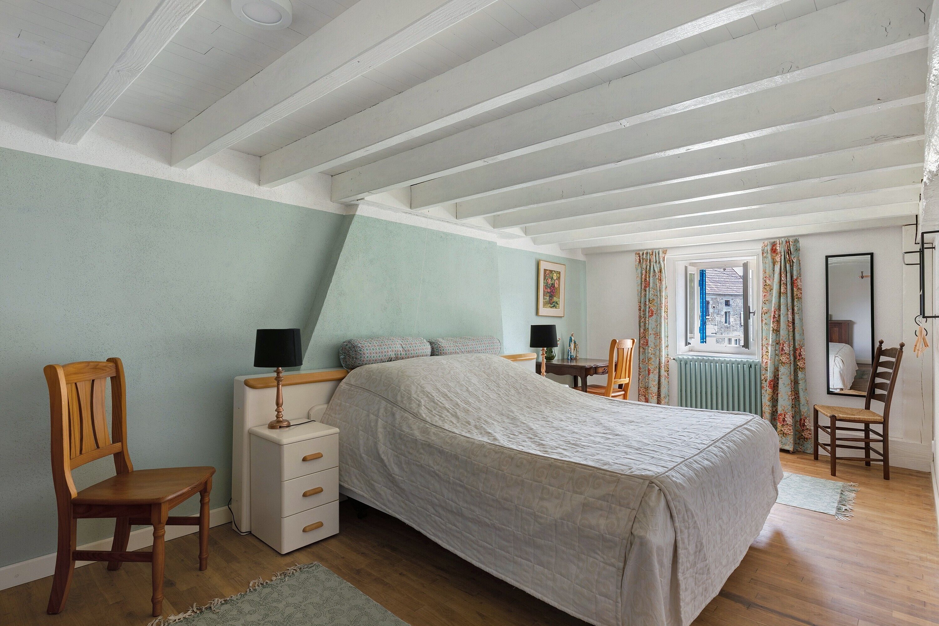 A bedroom with a bed, a dresser, a chair, a table, and a window with curtains.
