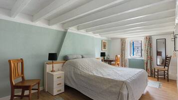 A bedroom with a bed, a dresser, a chair, a table, and a window with curtains.