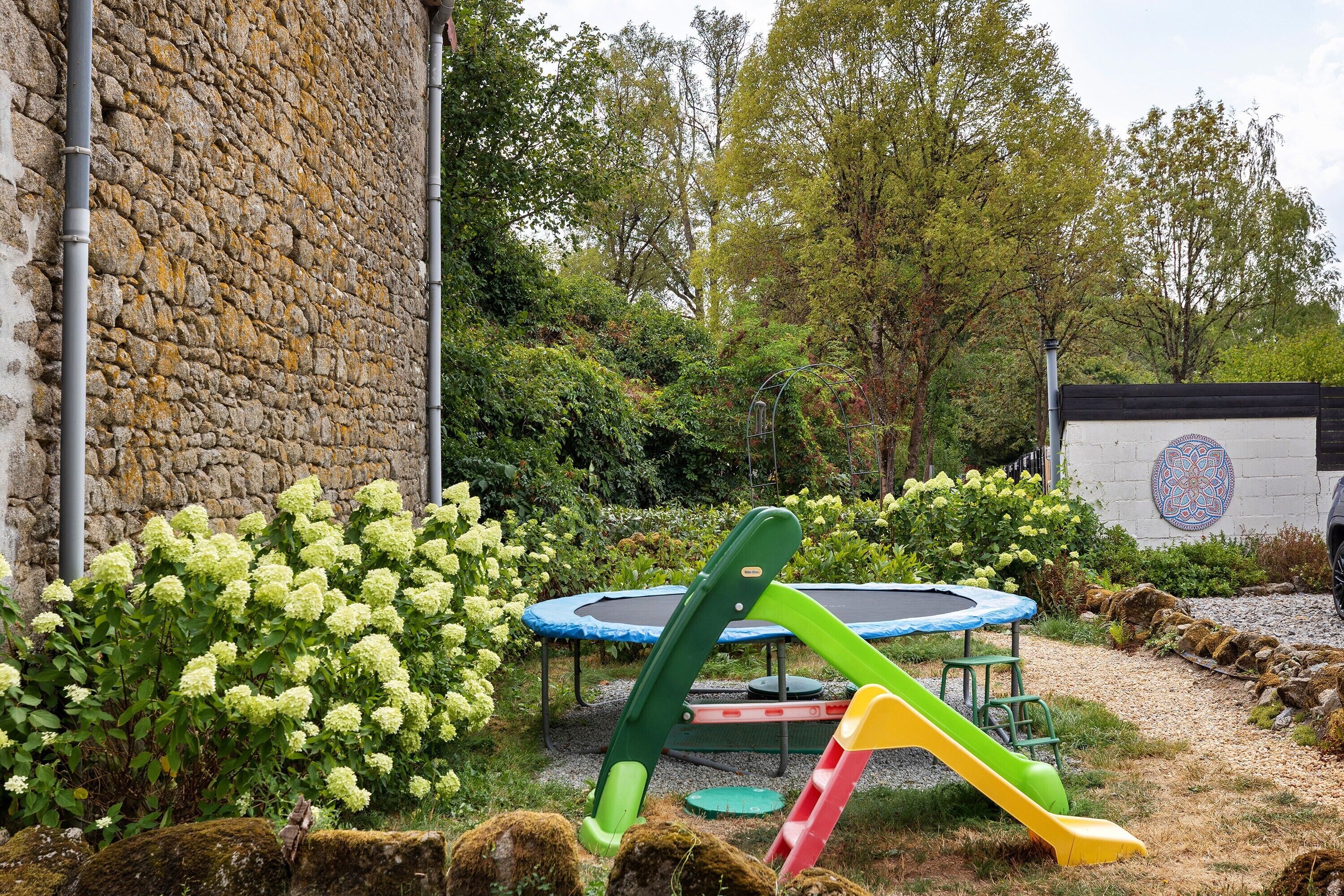 A garden with a stone wall, a trampoline, and children's play equipment.