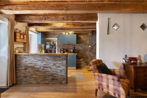 A rustic kitchen with exposed wooden beams, a stone island, and a blue cabinet.