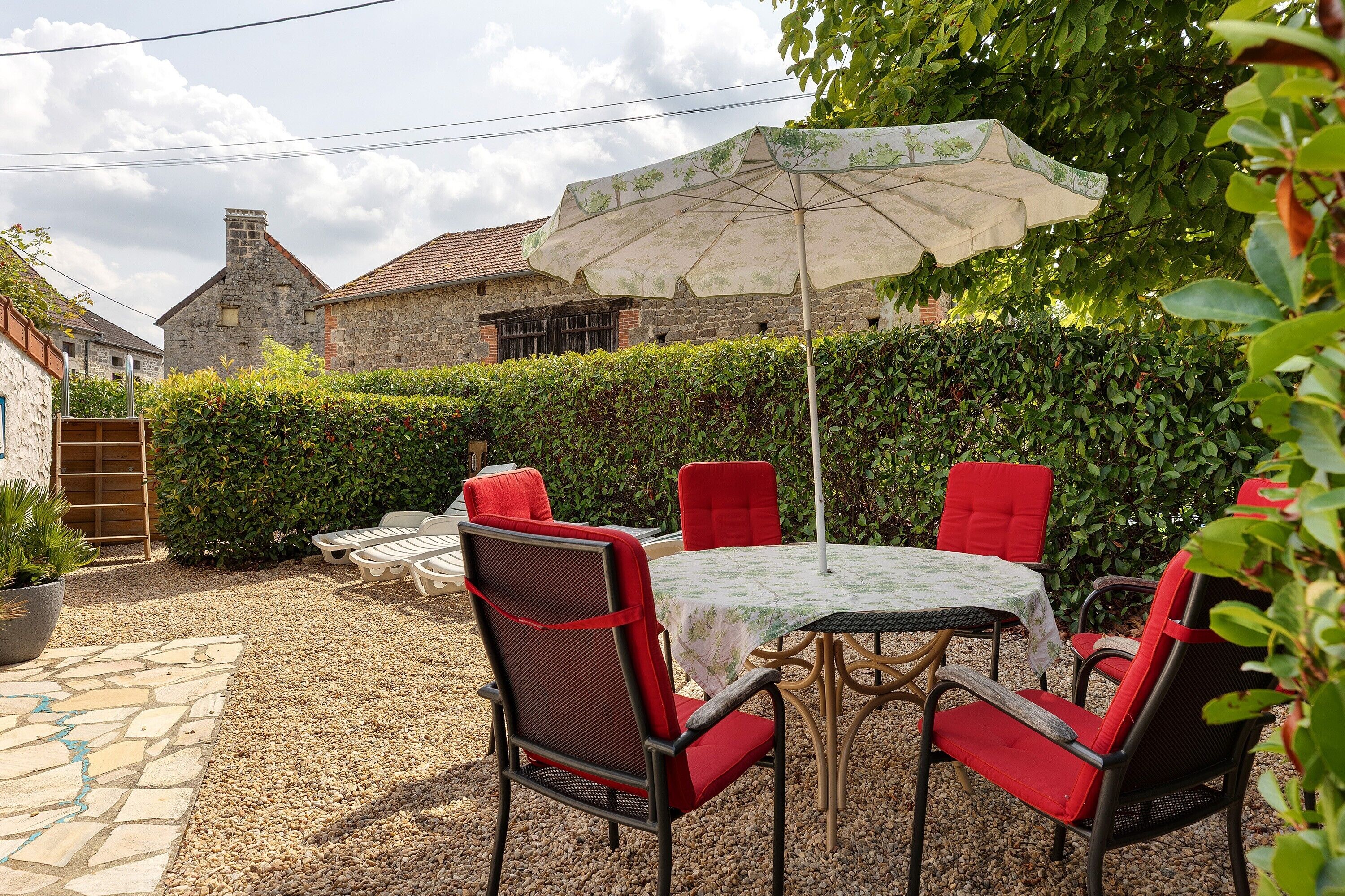 Eine Terrasse mit Tisch und Stühlen, einem großen Sonnenschirm und einem Steinhaus im Hintergrund.