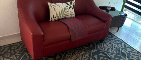 A red leather sofa with a patterned throw blanket and a decorative pillow, placed on a patterned rug.