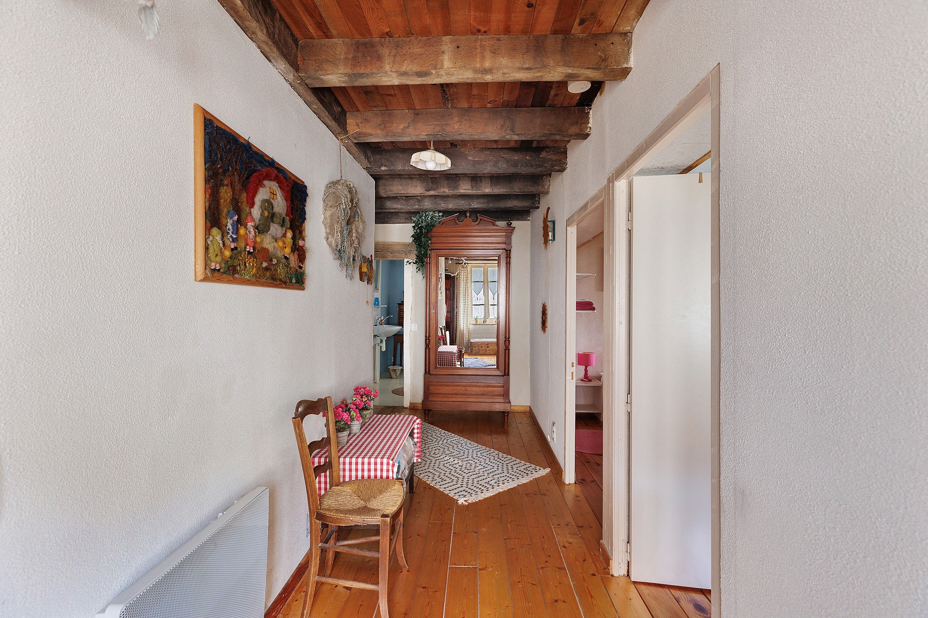 Un corridoio stretto con pavimento in legno, una sala da pranzo con tovaglia a quadretti e una porta che dà su un'altra stanza.