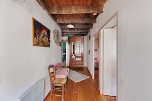 A narrow hallway with wooden flooring, a dining area with a checkered tablecloth, and a door leading to another room.