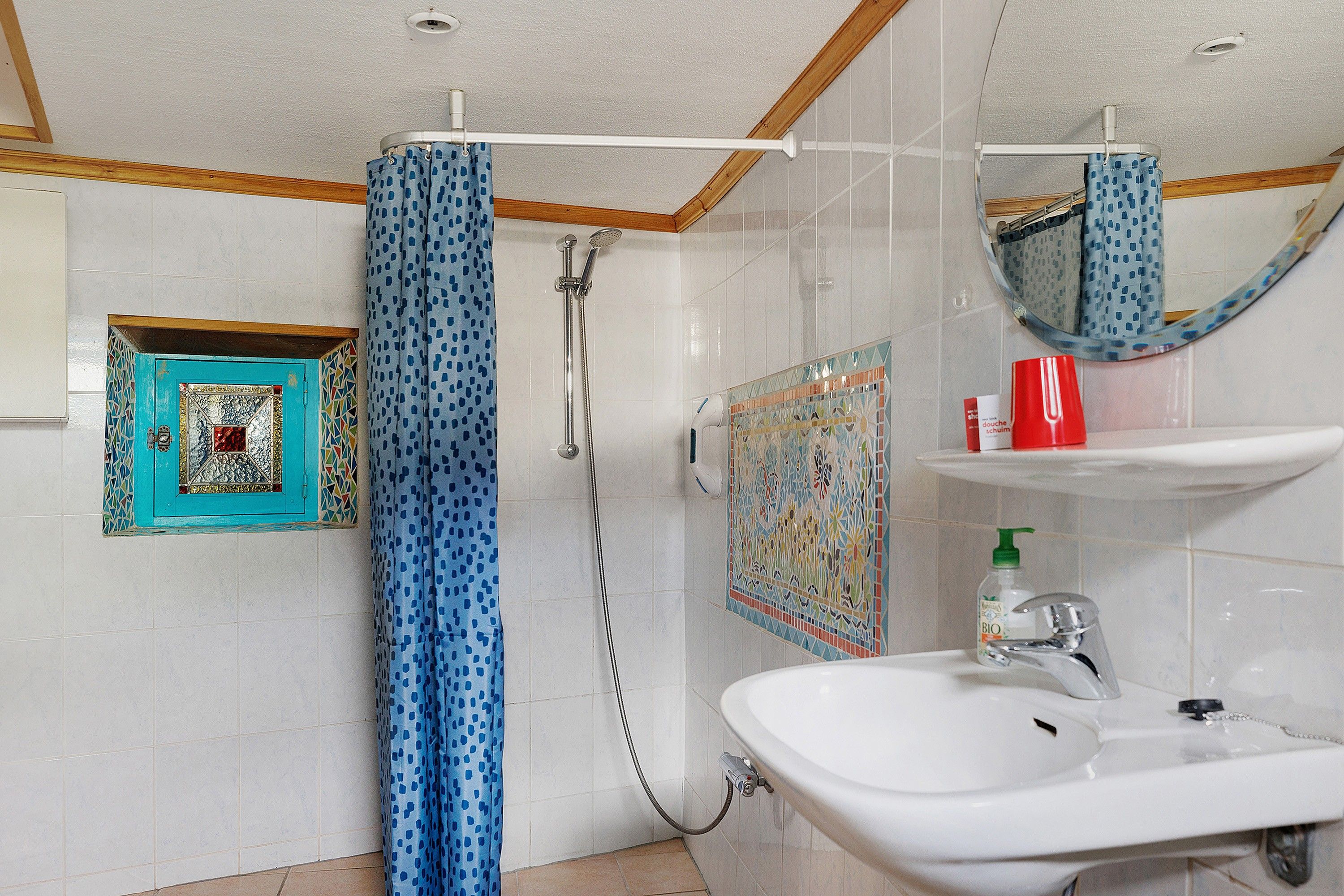 Ein Badezimmer mit Dusche, Waschbecken, Spiegel und Ablage für Toilettenartikel.