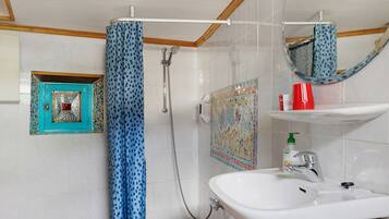 Ein Badezimmer mit Dusche, Waschbecken, Spiegel und Ablage für Toilettenartikel.