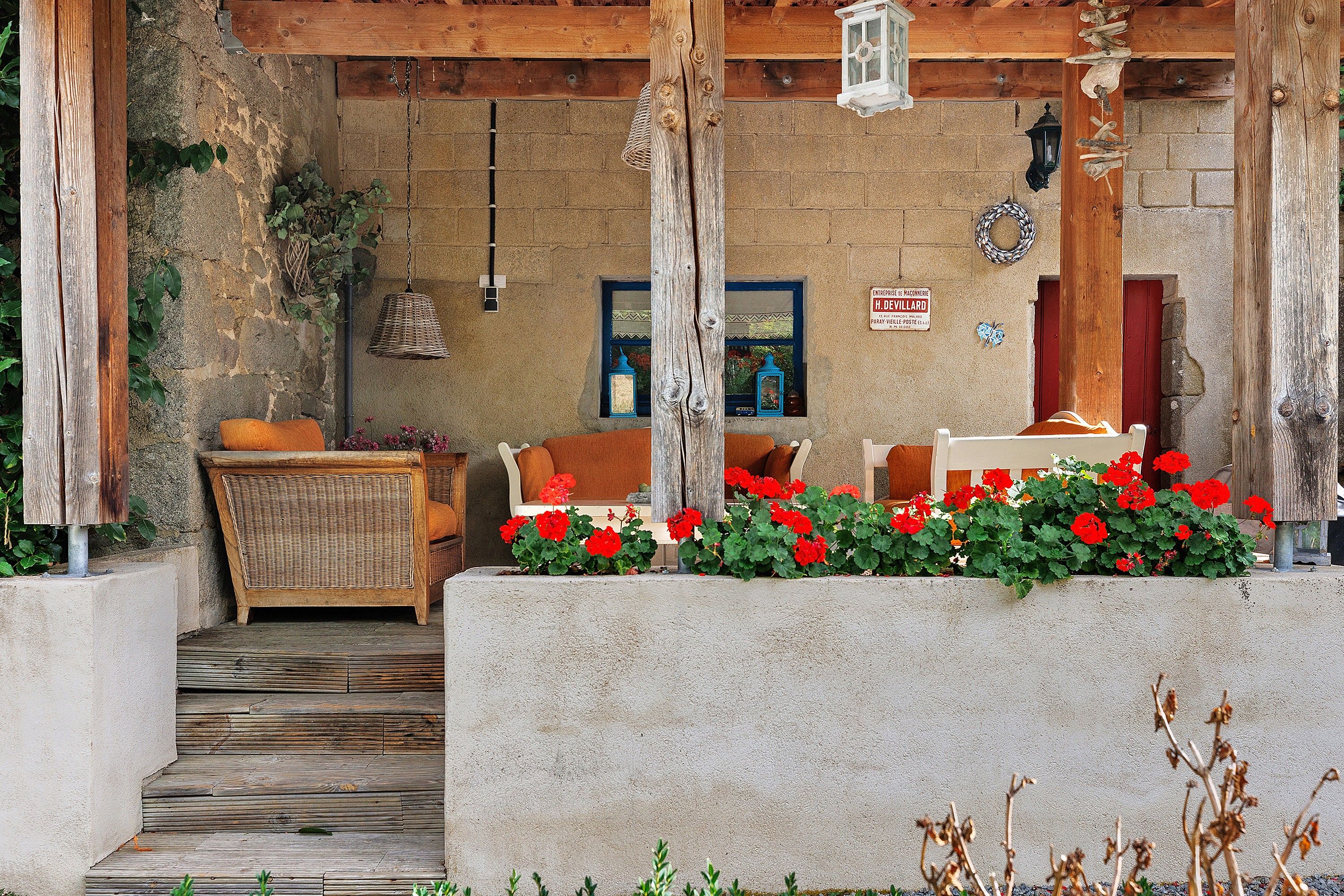 Un espace extérieur aménagé dans un style rustique, avec des meubles en osier et des fleurs rouges.