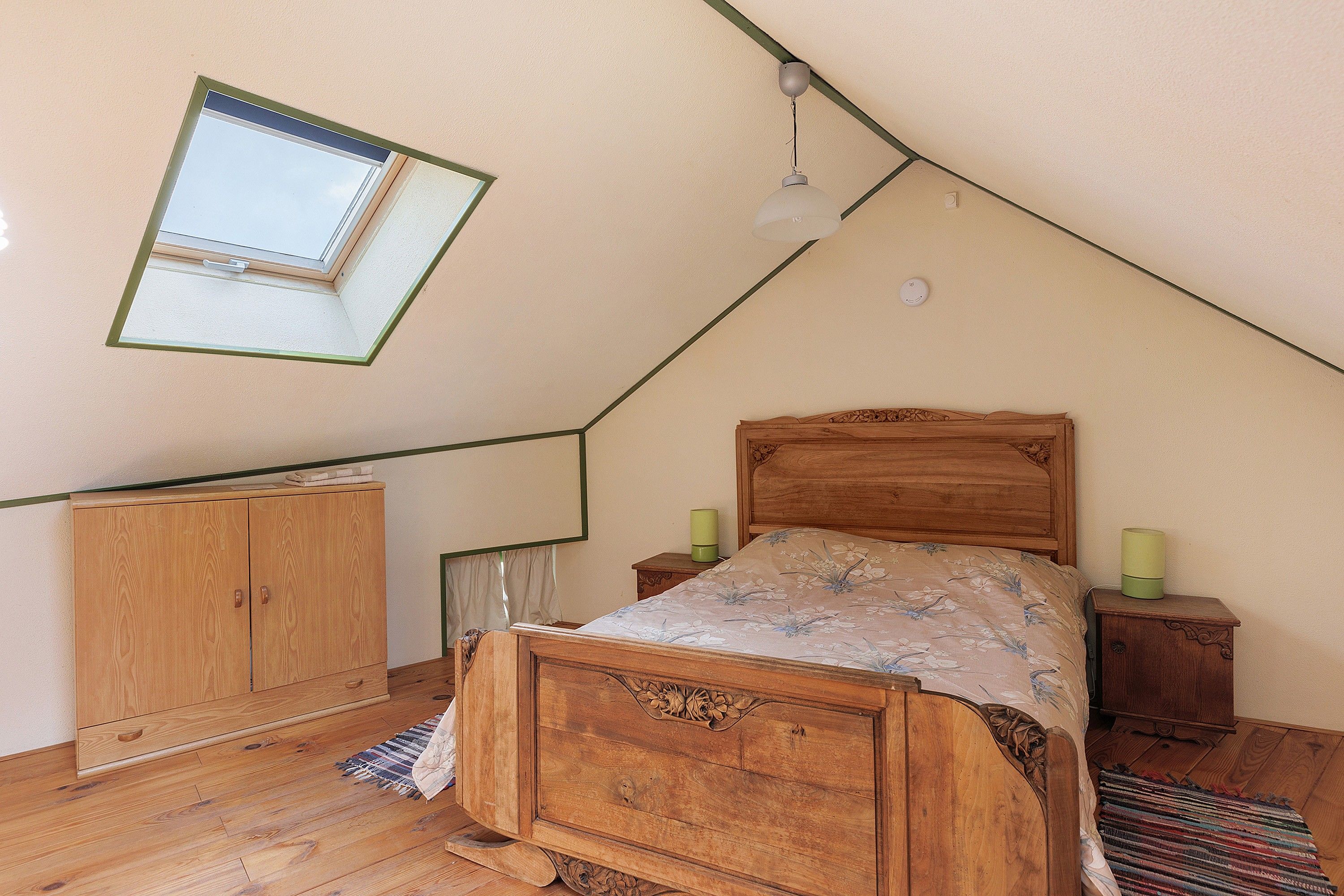A bedroom with a sloped ceiling, a wooden bed, a nightstand, a wardrobe, and a skylight.