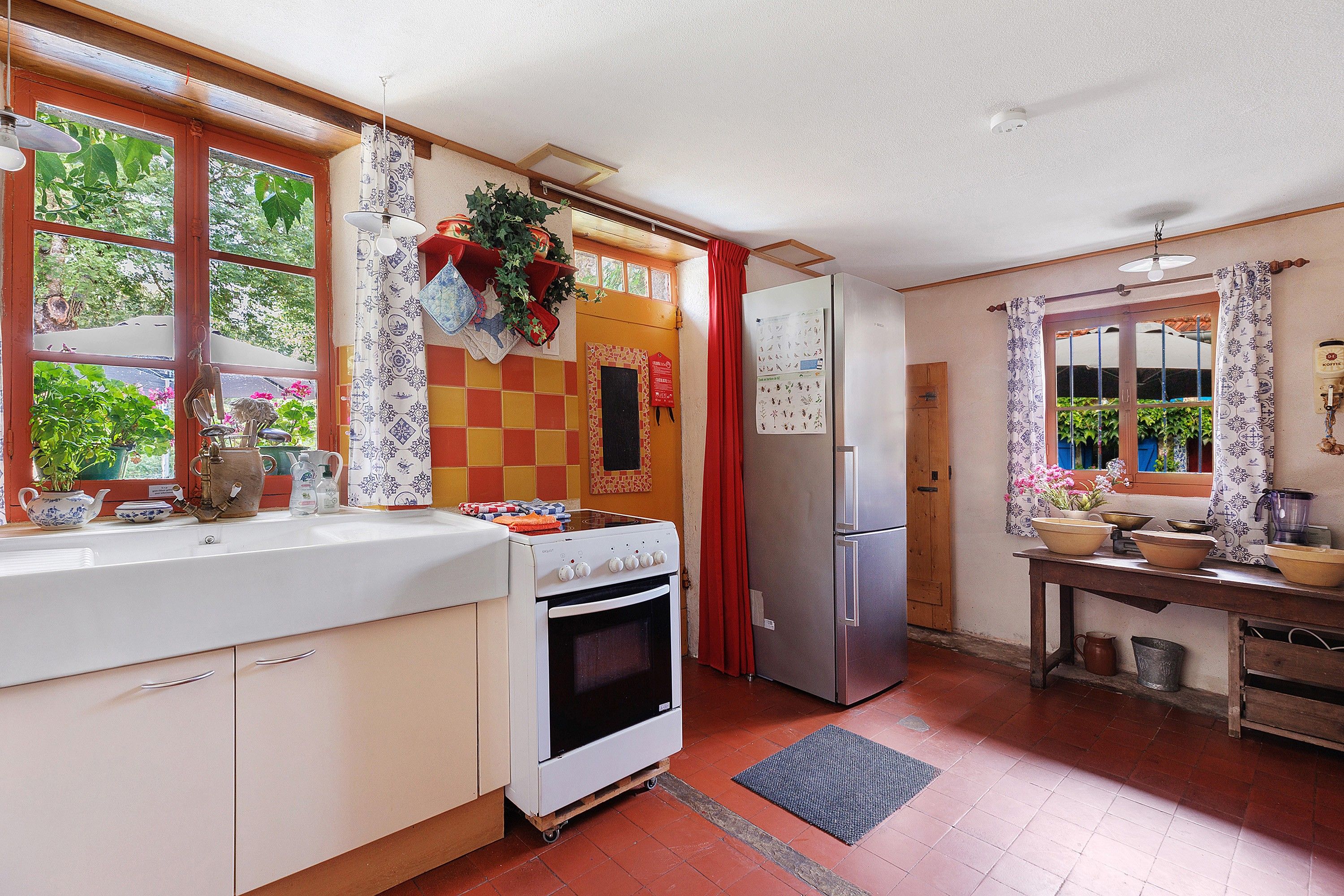 Una cucina con piano cottura, forno, frigorifero e una finestra con tende.