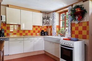 Une cuisine avec des meubles blancs, un fourneau et une fenêtre avec un rideau.