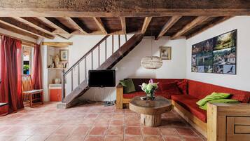 A cozy living room with a wooden staircase, a flat-screen TV, a red sofa, and a wall with framed pictures.