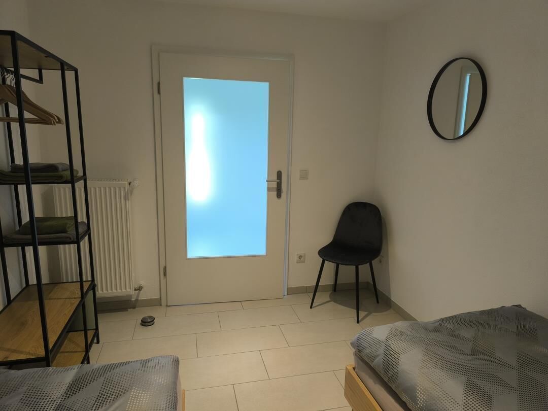 Ein Zimmer mit einem Bett, einem Sessel, einer Heizung, einer Tür und einem Spiegel an der Wand.