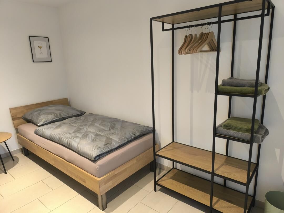 A bedroom with a bed, a small table, a wardrobe with shelves, and a framed picture on the wall.