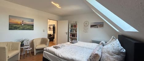 Un dormitorio con cama, una silla, una mesita, una estantería y un tragaluz.