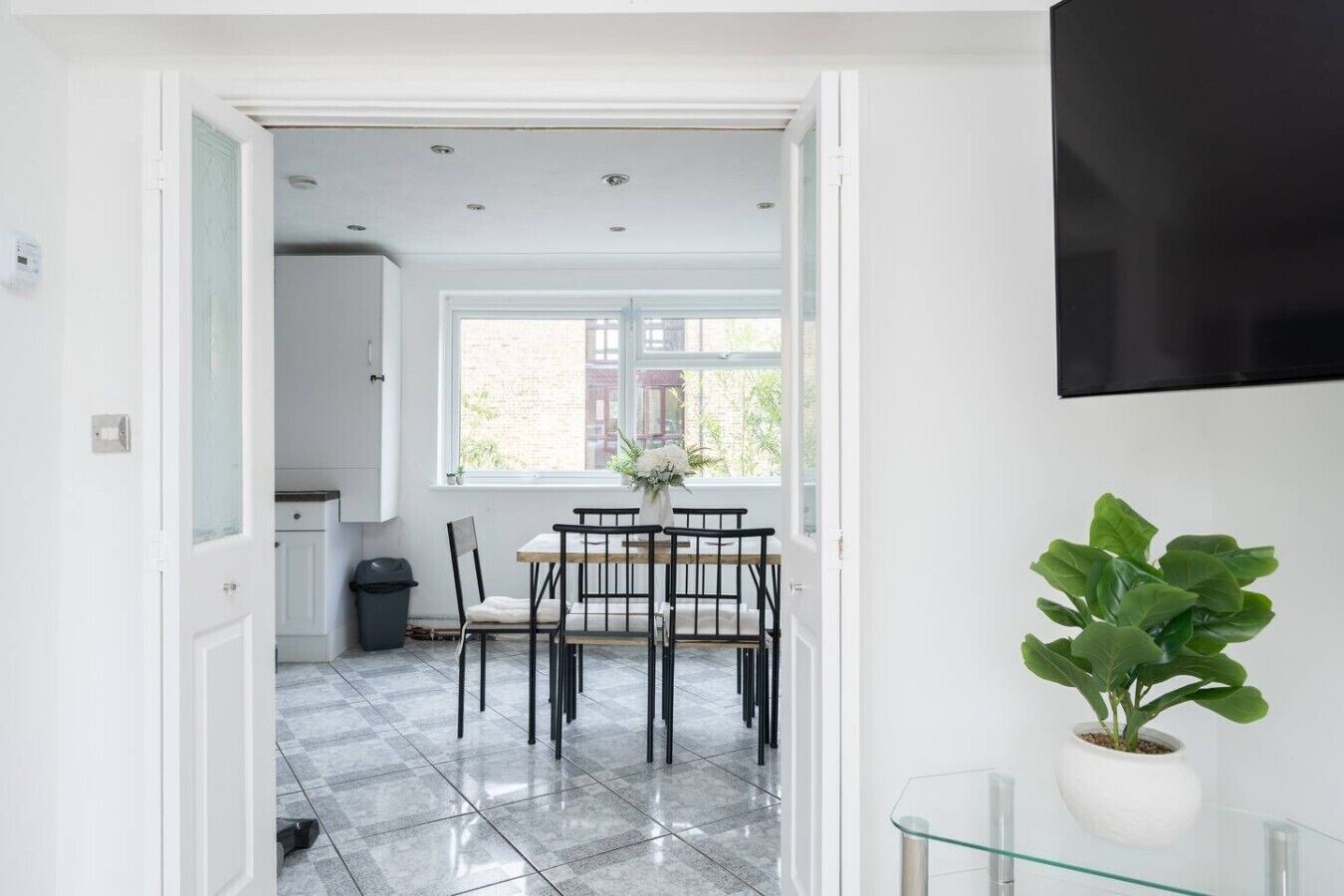 A dining area with a table and chairs, a potted plant, and a TV mounted on the wall.