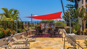 Un patio al aire libre con una parrilla, una zona de estar y una vela de sombra roja.