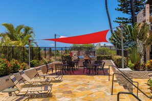 An outdoor patio with a barbecue grill, seating area, and a red shade sail. - Ocean View Retreat - Walk to Kamaole Beach - Spacious Lanai (Kihei)