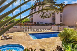 A swimming pool with lounge chairs, a building with balconies, and tropical plants. - Ocean View Retreat - Walk to Kamaole Beach - Spacious Lanai (Kihei)