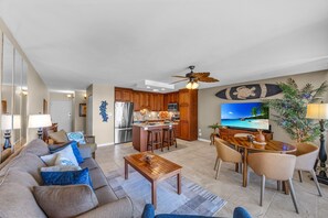 A modern living room with a sofa, coffee table, and dining area with chairs. - Ocean View Retreat - Walk to Kamaole Beach - Spacious Lanai (Kihei)