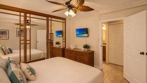 Un dormitorio con cama, cómoda, televisor y ventilador de techo.