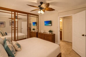 A bedroom with a bed, a dresser, a television, and a ceiling fan. - Ocean View Retreat - Walk to Kamaole Beach - Spacious Lanai (Kihei)