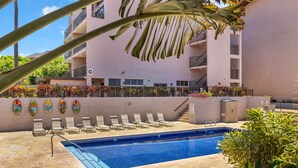 Una piscina con sillas de descanso, una terraza de baldosas de piedra y un edificio con balcones.