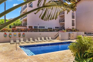 A swimming pool with lounge chairs, a stone-tiled deck, and a building with balconies. - Ocean View Retreat - Walk to Kamaole Beach - Spacious Lanai (Kihei)