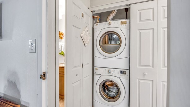 Un cuarto de lavandería con dos lavadoras apiladas y una secadora, puertas blancas y un calentador de agua visible.