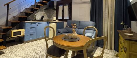A compact living space with a dining area, a sofa, a staircase, and a kitchen area.