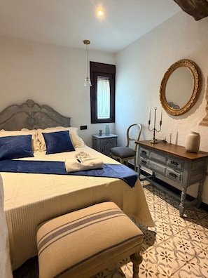 A bedroom with a bed, a dresser, a mirror, a window, and a lamp. - The Jewel of Setenil - Zafiro Cave House (Setenil de las Bodegas)