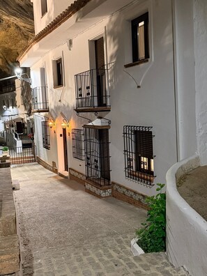 A building with multiple windows, some with metal bars, a staircase leading to an upper level, and a small garden area. - The Jewel of Setenil - Zafiro Cave House (Setenil de las Bodegas)
